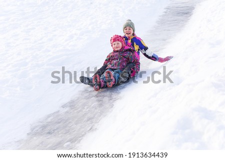 Winter activities outdoors. Cute happy little girls wearing a warm clothes are having fun, sliding down a hill on the ice slide