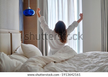 Back view of lazy woman wearing bathrobe wake up from good sleep in early morning during relaxing at cozy comfort bedroom at hotel room. Easy lifestyle. Start new day Royalty-Free Stock Photo #1913642161