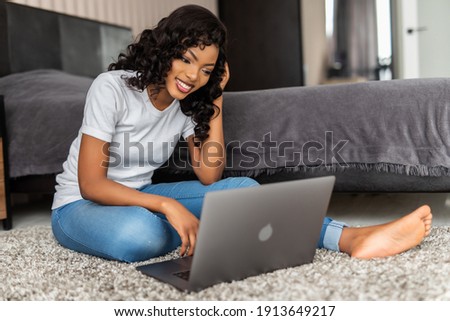 Portrait of happy young afro american woman use laptop while sitting on a floor with legs crossed in bedroom