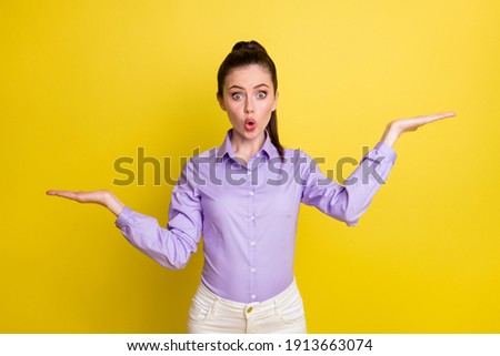 Photo portrait of impressed girl holding two blank spaces in hands one higher isolated on bright yellow colored background