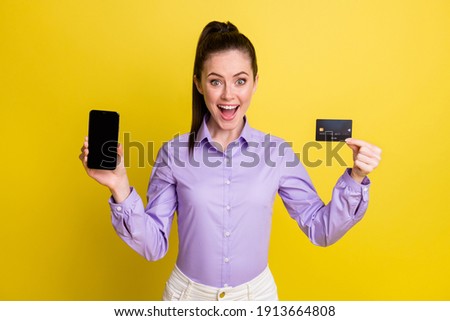 Photo of amazed girl open mouth hold card phone screen empty space wear purple shirt isolated yellow color background
