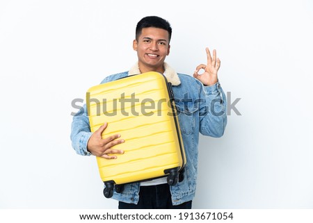 Young Ecuadorian man isolated on white background in vacation with travel suitcase and making OK sign