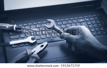 Male hand showing wrench over computer keyboards. IT Service. Support