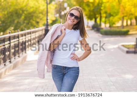 Attractive blonde Caucasian young woman wearing casual clothes and sunglasses enjoys posing during a walk in a autumn park in the day. Portrait of an attractive and happy girl.