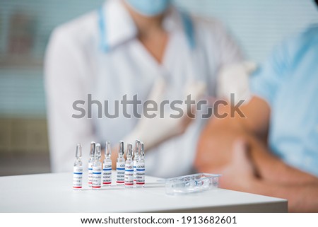 Close-up of vaccine vials. Female doctor with surgical mask and in gloves giving vaccine injection to man in hospital. Vaccination during COVID-19 pandemic