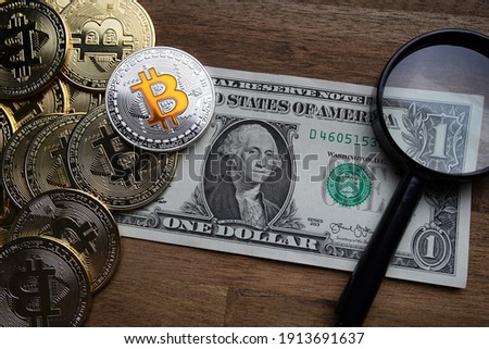 Pile of american dollars cash on brown wooden table. Next to it are several gold bitcoin digital cryptocurrency coins and a magnifying glass. Bank image and photo background.
