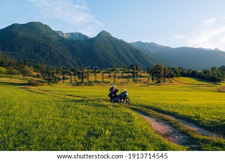Man motorcyclist ride touring motorcycle. Alpine mountains on background. Biker lifestyle, world traveler. Summer sunny sunset day. Green hills. hermetic packaging bags. copy space. Slovenia