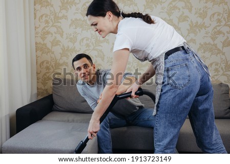 Wife vacuums the room and prevents her husband from watching TV