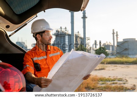 Refinery industry engineer watching blueprint for checking and working against oil refinery background,Concept to professional engineer on industrial.