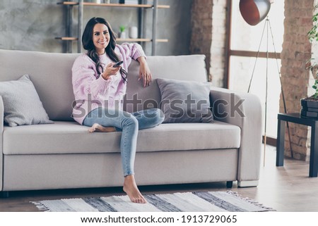 Full length photo of positive attractive young woman sit sofa watch tv switch channel indoors inside apartment