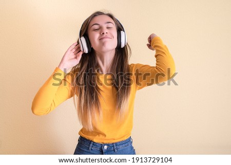 Young woman with headphones dancing on yellow background
