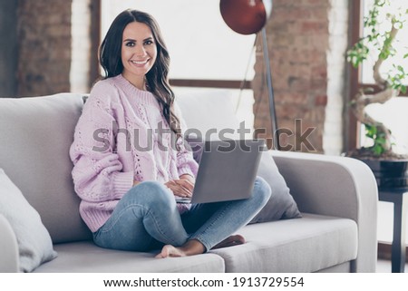Full body photo of stunning happy pretty young woman sit sofa hold computer remote work indoors inside apartment