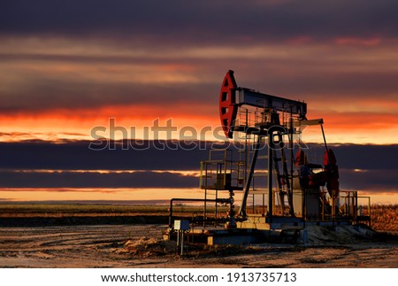 Crude oil pump jack at oilfield on sunset backround. Lorry driven on highway. Out of focus, possible granularity, motion blur

