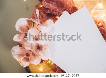 Top view blank white card and flowers on wooden plate or board on grey table background. Modern minimalist template.  