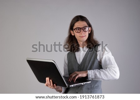 Programming and writing code, developing software products. Geek guy, with long hair and glasses, holding a laptop, gray background
