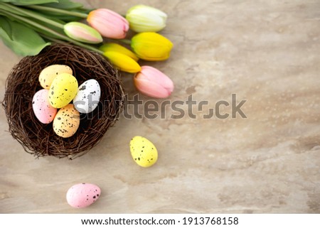Colorful easter quail eggs in nest and tulips on beige stone background with . Flat lay. Spring composition. Happy easter greeting card. Copy space