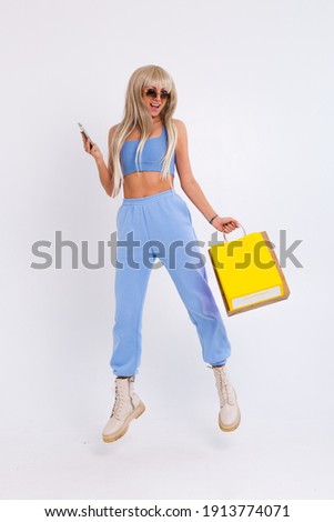 Fashion portrait of young happy blonde woman with long gorgeous straight hair hold colorful shopping bags and mobile phone in the studio on a white background. 