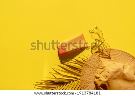 White and Yellow Palm Branches, bucket sun hat, SPF sunblock cream, yellow sunglasses on yellow background. Hard shadows. Summer banner template flat lay. Text space. Trendy Sun protection accessory.