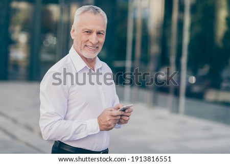 Photo of good mood smiling age businessman wear white shirt typing modern gadget outside city street