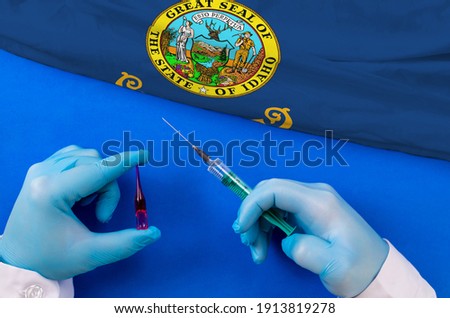 Idaho Vaccination. Hands of doctor holding syringe and coronavirus (COVID-19) vial vaccine on flag Idaho