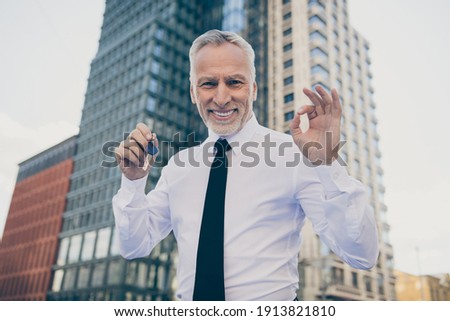 Photo of optimistic old business man hold key show okey sign wear white shirt outdoors near work center