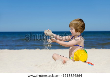 Little girl in swimsuit playing on a sandy beach, blue sea in the background