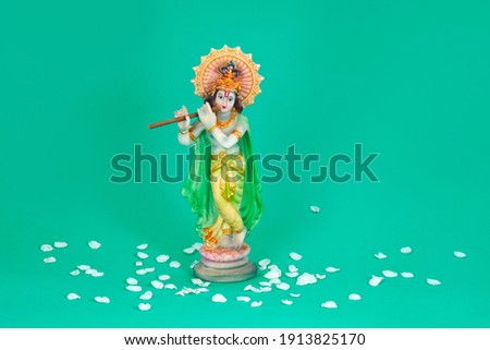 Hindu god Krishna. Statue with white petals on a green background.