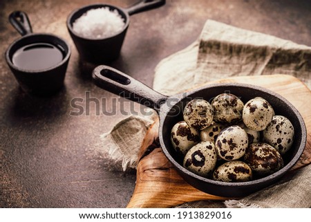 Black frying pan with quail eggs on wooden cutting board. Colorful eggs, diet food.