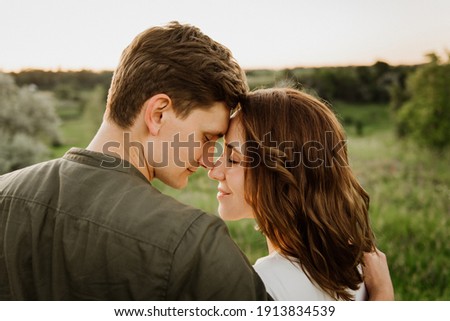 Young beautiful woman and man hug, kiss and walk in nature at sunset. Royalty-Free Stock Photo #1913834539