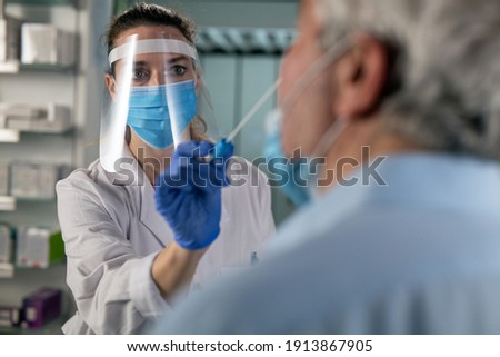 Cinematic shot of female pharmacist with medical mask is making nasopharyngeal swab test of coronavirus to male patient in pharmacy. Concept: covid-19, protection, safety, pandemic, prevention, assistance Royalty-Free Stock Photo #1913867905