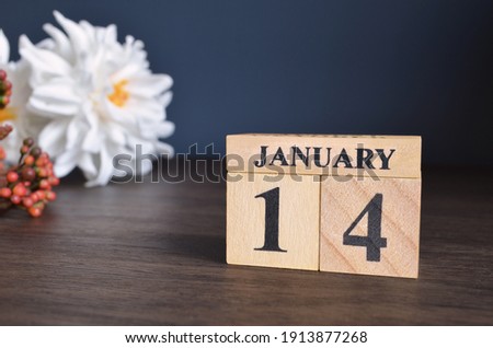 January 14, Date cover design with calendar cube and white Paeonia flower on wooden table and blue background.