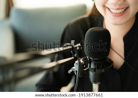 Happy Asian woman setting up a living room in her house for podcast studio, woman arranging a podcast and online radio station at home. Professional young podcaster speaking through a microphone.