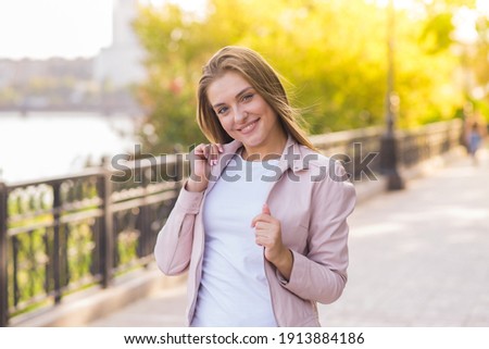 Portrait of an attractive and happy blonde Caucasian young woman in casual clothes pink jacket during a walk in the park on a warm spring day.