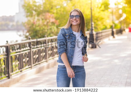 Portrait of a happy and attractive blonde Caucasian young woman in a casual denim jacket outdoors in a park on a sunny autumn day. A concept of lifestyle, happiness and joy.