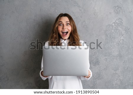 Happy excited young woman in casual clothes using laptop computer isolated on a gray background