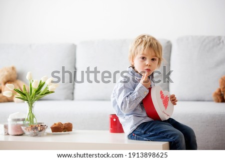 Beautiful blond boy, giving mother flowers and box with little gift for mothers day at sunny living room
