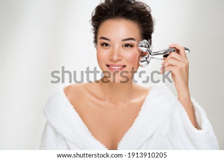 Attractive woman massaging her cheek with massage Y-shaped ball roller on light blue background. Beauty and Skin care concept. Plus size model