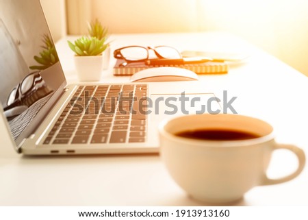 soft focus of keyboard laptop computer on desk table office, coffee cup and notebook, glasses. Business and finance concept. Workplace with morning sunlight from the window with copy space.