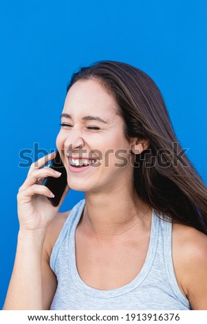Portrait of a beautiful young woman laughing and talking on the phone with blue wall