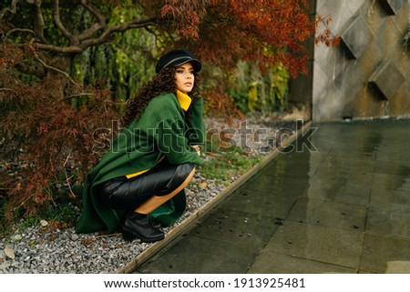 In the park at the backwater squatted stylish beautiful girl in warm clothes and looks into the distance. High quality photo