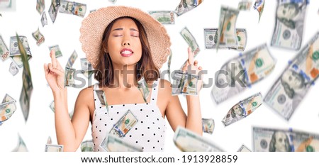 Young beautiful chinese girl wearing summer hat gesturing finger crossed smiling with hope and eyes closed. luck and superstitious concept.