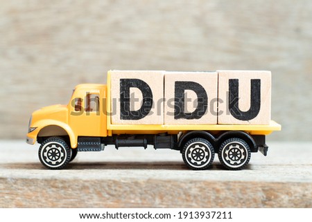 Toy truck hold alphabet letter block in word DDU (abbreviation of Delivered Duty Unpaid) on wood background