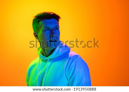 Dreamful. Caucasian man's portrait isolated on yellow studio background in mixed neon light. Handsome male model. Concept of human emotions, facial expression, sales, ad, fashion. Copyspace.