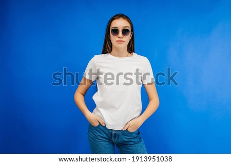 Stylish girl in glasses wearing white t-shirt posing in studio on blue background