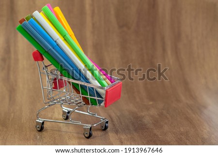 Small shopping cart with colored pencils on dark wooden background close up