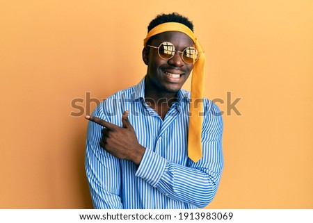 Handsome black man drunk wearing tie over head and sunglasses cheerful with a smile of face pointing with hand and finger up to the side with happy and natural expression on face 