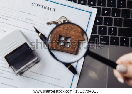 Wooden house, magnifying glass and contract on a laptop. Concept of rent, search or mortgage. Close-up
