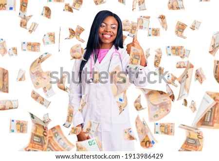 Young african american woman wearing doctor stethoscope looking proud, smiling doing thumbs up gesture to the side