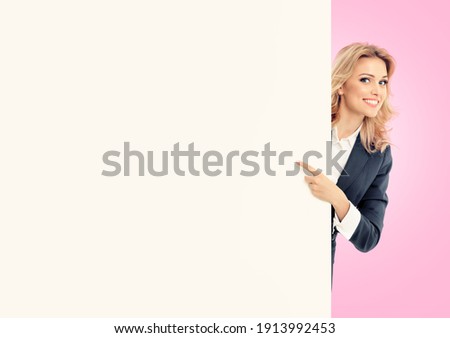Happy smiling pointing showing advertising businesswoman in grey confident suit, standing behind blank banner or signboard  with copy space for some ad slogan text, isolated over pink color background