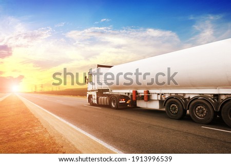 Big metal fuel tanker truck shipping fuel on the countryside road against a night sky with a sunset Royalty-Free Stock Photo #1913996539
